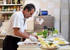 a man preparing food in a kitchen with plates of food at Hotel Aquamarin in Bad Mitterndorf