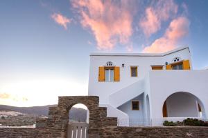 a white house with an archway against a cloudy sky at Pirgos Suites in Panormos