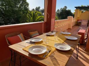 uma mesa de madeira com pratos e copos de vinho numa varanda em A charming 6-person apartment, golf, surfing, free tennis courts and bicycles em Isla Canela