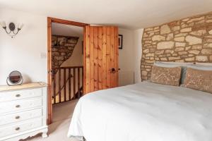 a bedroom with a white bed and a stone wall at Teasel Cross Cottage, Painswick in Stroud