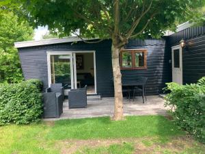a black house with chairs and a table and a tree at Chalet Wild Forest, knus chalet op de Veluwe met gratis parkeren in Putten