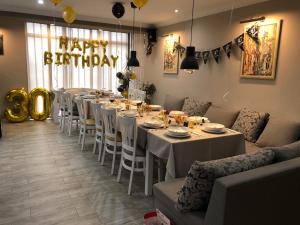 een lange eetkamer met witte tafels en een happy birthday bord bij Guesthouse Green Fields in Garmen