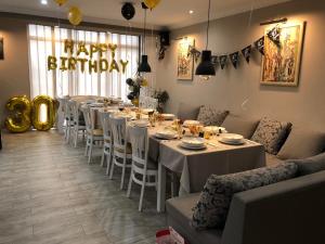 a long dining room with white tables and a happy birthday sign at Guesthouse Green Fields in Garmen
