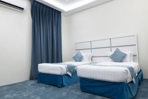 two beds in a room with blue curtains at Garden View Suites in Tabuk