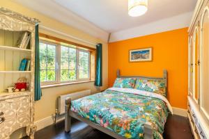 a bedroom with orange walls and a bed and window at Church Lane Cottage - Norfolk Holiday Properties in Filby