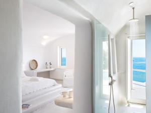a white bedroom with a view of the ocean at Mykonos Blu, A Grecotel Resort to Live in Psarou