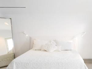 1 cama blanca con almohadas blancas y espejo en Mykonos Blu, Grecotel Boutique Resort, en Psarou