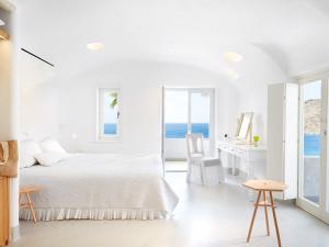 a white bedroom with a bed and a desk at Mykonos Blu, Grecotel Boutique Resort in Psarou