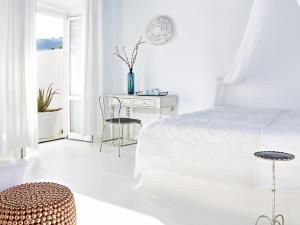 a white bedroom with a bed and a desk at Mykonos Blu, A Grecotel Resort to Live in Psarou