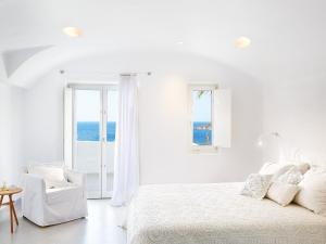 a white bedroom with a bed and a chair at Mykonos Blu, A Grecotel Resort to Live in Psarou