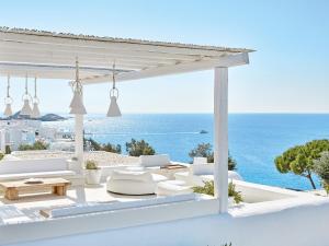 a patio with white furniture and a view of the ocean at Mykonos Blu, A Grecotel Resort to Live in Psarou