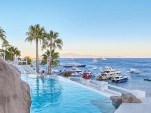 a pool at a resort with boats in the water at Mykonos Blu, A Grecotel Resort to Live in Psarou
