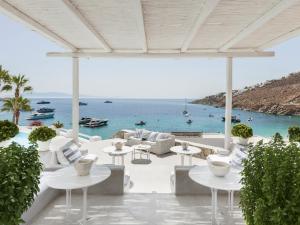 a patio with white tables and chairs and the ocean at Mykonos Blu, A Grecotel Resort to Live in Psarou