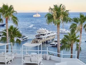 a balcony with palm trees and boats in the water at Mykonos Blu, A Grecotel Resort to Live in Psarou
