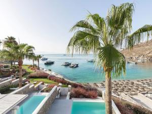 a palm tree and a swimming pool next to the ocean at Mykonos Blu, A Grecotel Resort to Live in Psarou