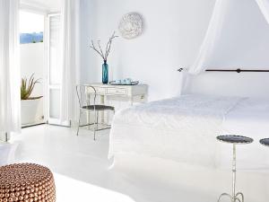 a white bedroom with a bed and a table at Mykonos Blu, A Grecotel Resort to Live in Psarou