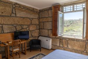 a room with a stone wall with a desk and a window at Quinta do Reconco in Santa Eugénia