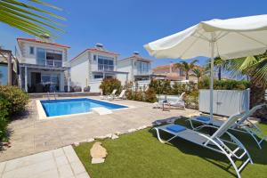 a villa with a swimming pool and two chairs and an umbrella at Villa Aphrodisia - Seafront in Ayia Napa