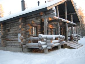 una cabaña de madera en la nieve con un montón de troncos en Revontuli Cottage, en Kolari