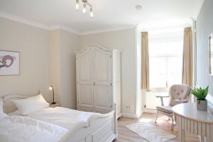 ein weißes Schlafzimmer mit einem Bett, einem Tisch und einem Stuhl in der Unterkunft Villa Gudrun in Westerland