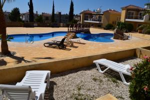 uma piscina com duas cadeiras brancas e um escorrega em Sirena Olympia Apartment 40 em Pafos