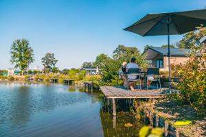 two people sitting at a table with an umbrella next to a lake at EuroParcs Zilverstrand in Mol