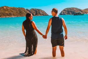Un uomo e una donna in piedi sulla spiaggia di Varandas do Arraial- Hostel ad Arraial do Cabo