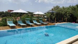 a swimming pool with blue chairs and umbrellas at villa Orchidee Sardegna in Capitana