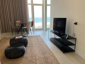 sala de estar con TV y mesa con sillas en Porto Covo Praia Hotel & SPA, en Porto Covo