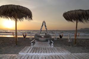 um banco na praia com dois guarda-sóis em Pelagos Suites Hotel & Spa em Cidade de Kos