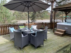 a table with chairs and an umbrella on a deck at Luxury Riverside Lodge, Blair Atholl in Pitlochry