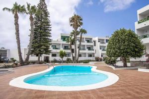 a swimming pool in front of a building with palm trees at Holyhome premium 105 in Costa Teguise