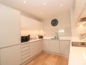 una cocina con armarios blancos y un reloj en la pared en 5 The Manor House, Hillfield Village en Dartmouth