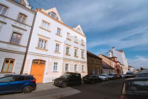 un bâtiment blanc avec une porte orange à côté des voitures garées dans l'établissement Pilsner Apartments, à Plzeň