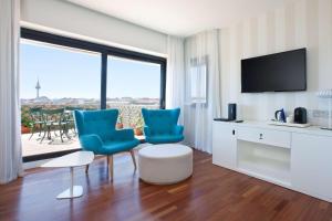 un salon avec deux chaises bleues et une télévision dans l'établissement NH Madrid Ventas, à Madrid