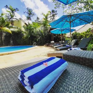 a pool with chairs and umbrellas next to a swimming pool at Sama's Cottages and Villas in Ubud