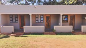 a house with white walls and doors and grass at Hluzu Guest House in Hluhluwe