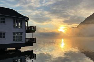 a house on the water with the sunset in the background at Skjolden Resort in Skjolden