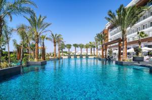 a swimming pool with palm trees in front of a building at Amanti, MadeForTwo Hotels - Ayia Napa in Ayia Napa