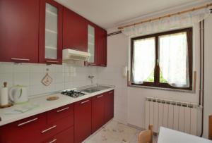 uma cozinha com armários vermelhos, um lavatório e uma janela em Apartment Luna em Poreč