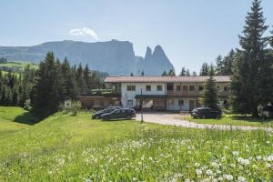 un bâtiment avec des voitures garées dans un champ de fleurs dans l'établissement Ferienparadies Sabina Santner, à Alpe di Siusi