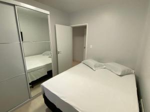 een slaapkamer met een wit bed en een spiegel bij Quadra do Mar Balneário Camboriú in Balneário Camboriú
