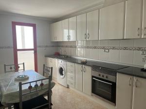 a kitchen with white cabinets and a table and a washing machine at ROMI CENTRO tu Alojamiento en TEULADA in Teulada