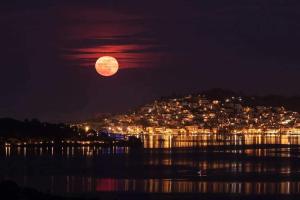 Ein Vollmond, der nachts über einer Stadt aufgeht in der Unterkunft Theodora Rooms in Poros