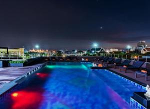 een zwembad 's nachts met een stad op de achtergrond bij Dang Derm In The Park Khaosan in Bangkok