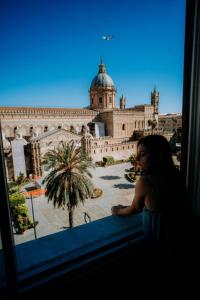 Una donna in piedi in una finestra che guarda fuori un edificio di Suite Cathedral Palermo a Palermo