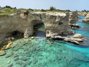an archway in the water next to a cliff at La maison del porto in San Foca +13 photos
