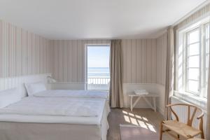 a white bedroom with a bed and a large window at Melsted Badehotel in Gudhjem