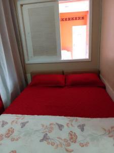 a bed with a red blanket and a window at Menina da Lua in Rio das Ostras