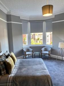 a bedroom with a bed and two chairs and windows at Ellwyn House in Edinburgh